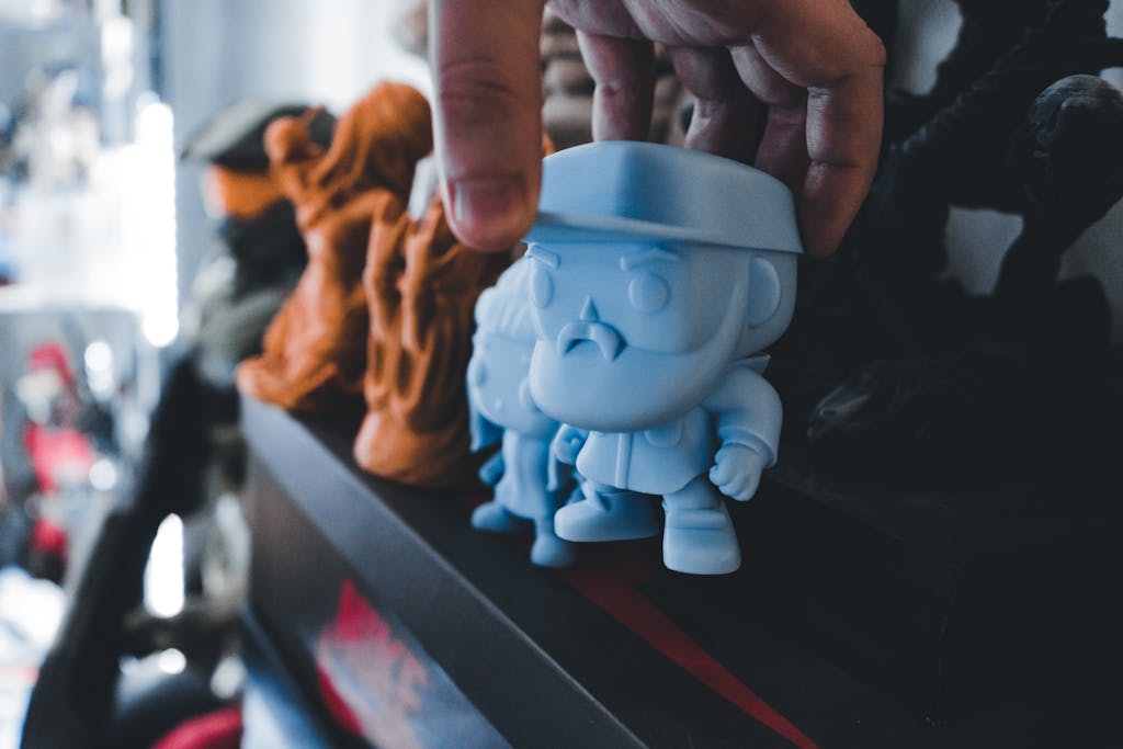 Close-up of a hand placing a blue toy figurine on a decorative shelf with other unique figurines.